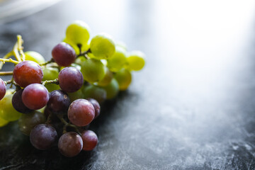 Green and purple organic grapes lie on a dark background. An organic grapes close-up. Fruits on a black background. Berries on a black marble table
