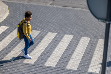 Curly-haired schoolboy crossing the street on a crosswalk