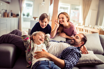 Happy young caucasian family being playful and having fun together on the couch in the living room...