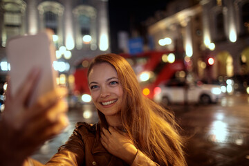 Happy young caucasian woman using a phone for a video call in the city at night