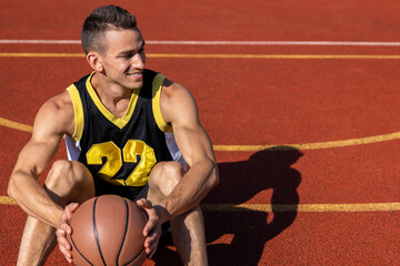 Cheerful man resting sitting on the basketball court after playing game.