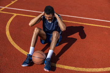 Black man doing sit ups and crunches exercising abdominal muscles outdoor on basketball court.