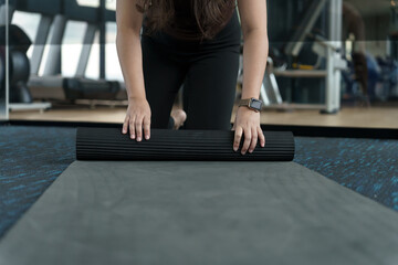 Fitness woman folding exercise mat before working out in yoga studio. rolling Yoga mat  after training healthy lifestyle