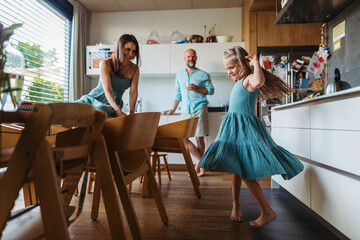 Little girl dancing in the kitchen, while parents watching her.