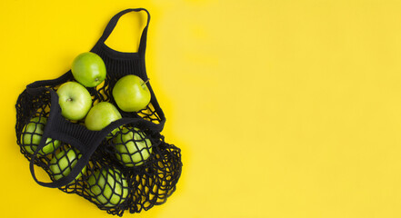 Mesh shopping black bag with green apples on the yellow background. Copy space. Top view.