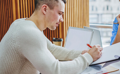 Young man designer drawing plan of sketch on paper collaborating with pretty colleague in office