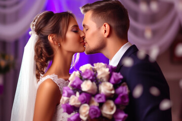 Wedding couple kissing and hugging in the room decorated with flowers in purple colors. - obrazy, fototapety, plakaty