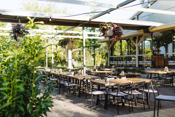 Fototapeta premium Covered summer terrace of a restaurant with wooden tables, chairs, and flooring.