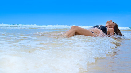 Woman in bikini  sunbathing and lying in waves on summer vacation beach.