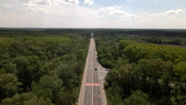 Straight road with 4 lanes surrounded by green forest, forward flyby drone on a summer day