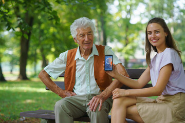 Caregiver helping senior diabetic man check his glucose data on smartphone outdoors, in park.