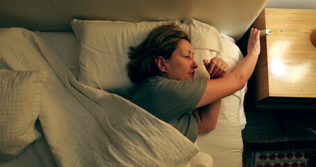 Thoughtful older woman switching lamp light OFF, person going to sleep
