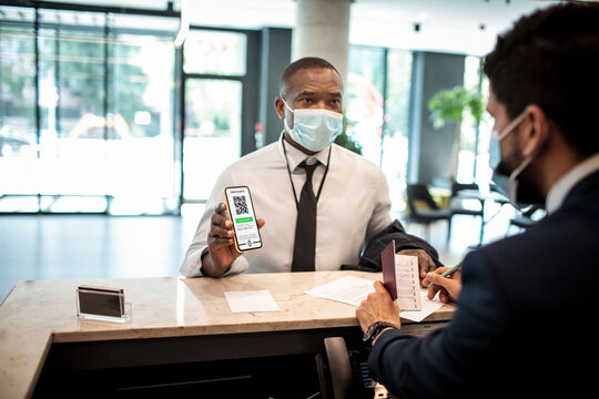 Young African American businessman showing the certificate of his vaccination on a smartphone at the reception of a hotel