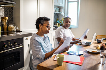 Senior African American woman going over bills and payments with her husband in the kitchen at home