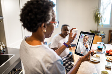 Senior African American woman asking for advice from her doctor about medication on a video call on the tablet in the kitchen at home