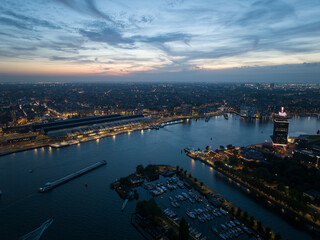 Aerial drone view of Amsterdam city skyline at night, Ij river, ferries, transportation over water. Railroad station and central landmarks and buildings.