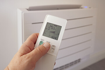 Human hand uses remote control, presses buttons, sets selects temperature of air cooling in home...