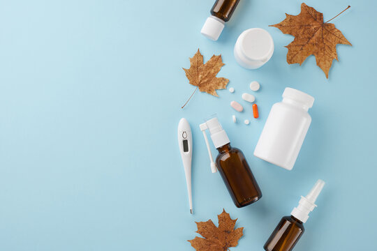 Scheduling a medical appointment for the fall. Top view flat lay of scattered pills, thermometer, nasal sprays, medicine mockups, dry maple leaves on light blue background with advert area