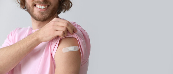 Young man with applied medical patch on grey background with space for text. Vaccination concept