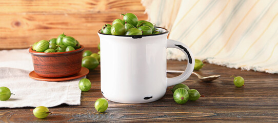 Mug and bowl with fresh gooseberries on wooden background