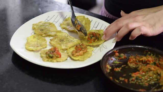 detailed view of a woman setting up a plate, pouring the stew on top of the flattened plantain. patacones with stew typical dish