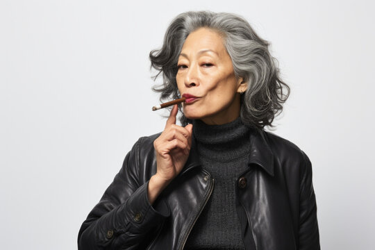 A woman is pictured wearing a leather jacket while smoking a cigarette. This image can be used to depict a rebellious or edgy lifestyle.