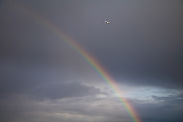 Rainbow and airplane on stormy dark sky background