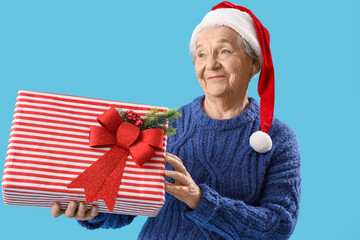 Obraz premium Senior woman in Santa hat with Christmas gift on blue background