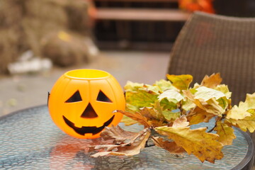 close-up of an orange pumpkin basket with a smiling face for sweets on a glass table for Halloween on the background of autumn decor in a cafe on the street