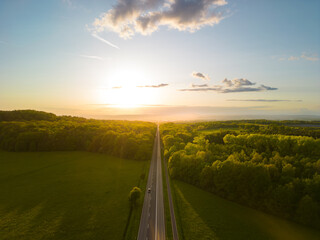 Aerial view of a straight road going through the forest at sunset - obrazy, fototapety, plakaty