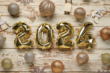 Figure 2024 made of foil balloons with Christmas balls on white wooden background