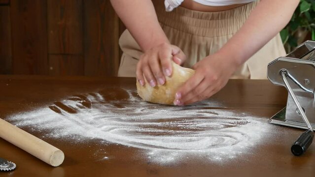 Young woman passionately kneads fresh dough for Italian pasta by hand. Unrecognizable female person making pizza or pasta dough.