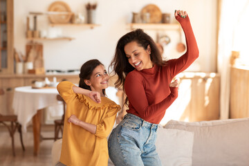 Cheerful mother and daughter moving and dancing to music indoor