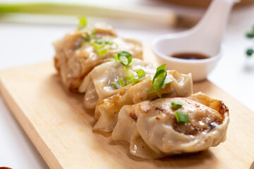 Close up of gyoza dumplings on a wooden board served with napkin, chopstick, sauce and ingredient on the side. white background. top view