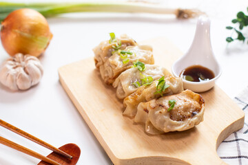 Close up of gyoza dumplings on a wooden board served with napkin, chopstick, sauce and ingredient on the side. white background. top view