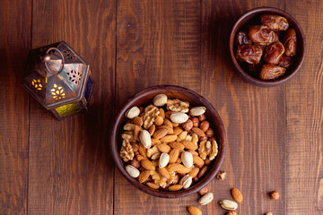 wooden bowl of nuts and dates on wooden background and lantern on side from top 