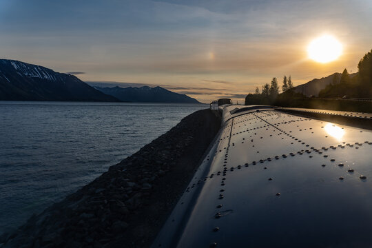 Alaska Railroad ride on the Turnagain Arm in Alaska at sunset. A sundog lights up the sky. The Coastal Classic track along the coastlines.  Low tide in extreme tidal area reveals mudflats. 