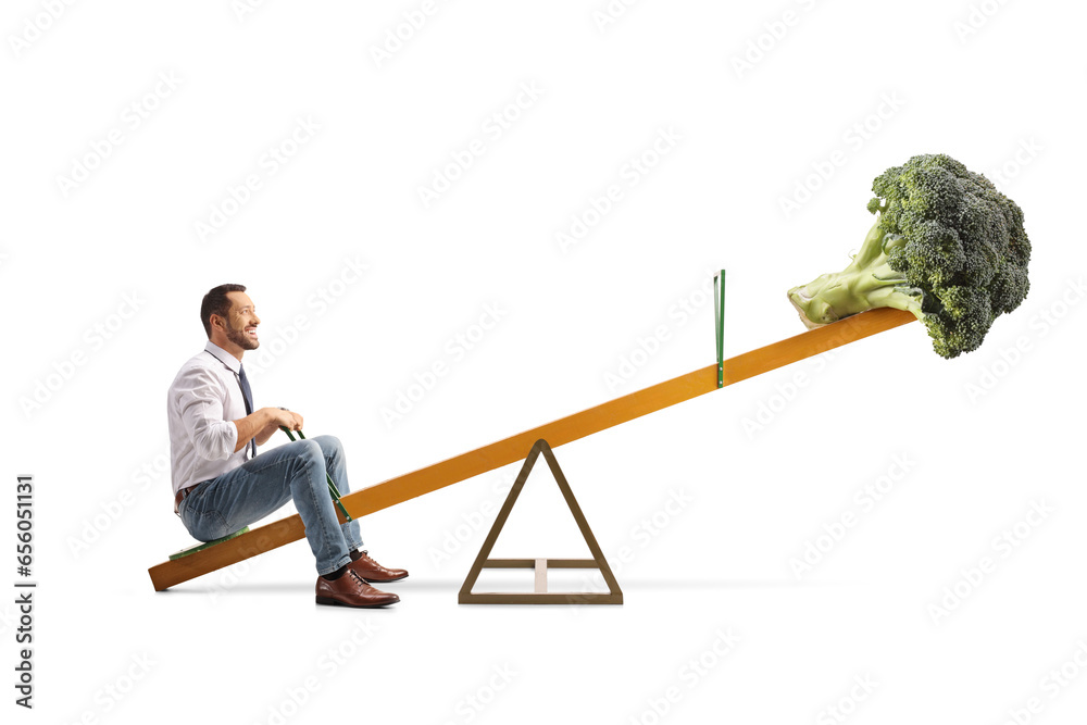 Wall mural Man sitting on a seesaw with broccoli, healthy diet concept