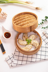 Gyoza dumplings cooked in bamboo steamer on white background served with napkin, chopstick, sauce and ingredient on the side. Top view, flat lay