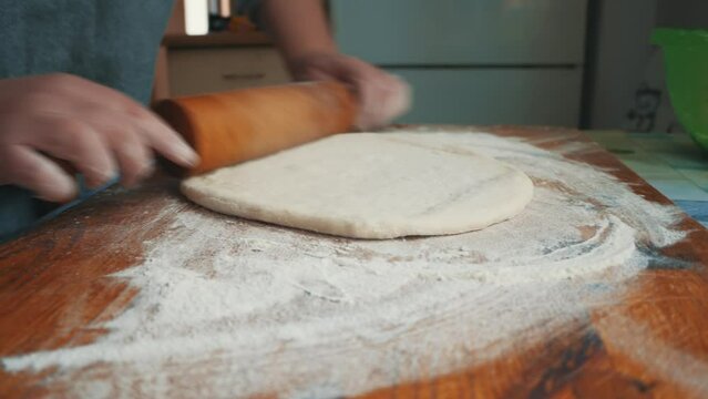 A young housewife kneads yeast dough on a wooden board. 