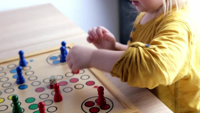 close-up of hands of small child manipulate with wooden figurines of family board game, smart kid, 2-year-old girl is learning to count, Cross and circle game Parcheesi, foreground focus