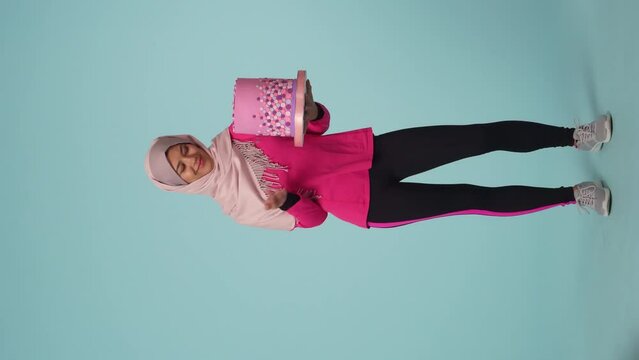 Full-sized isolated video capturing a young woman in a sportswear and a hijab, sheila choosing between a cake and an exercising mat, throwing a mat away.