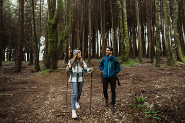 Fototapeta premium Positive young caucasian family in jackets with trekking sticks enjoy adventure, free time at weekend