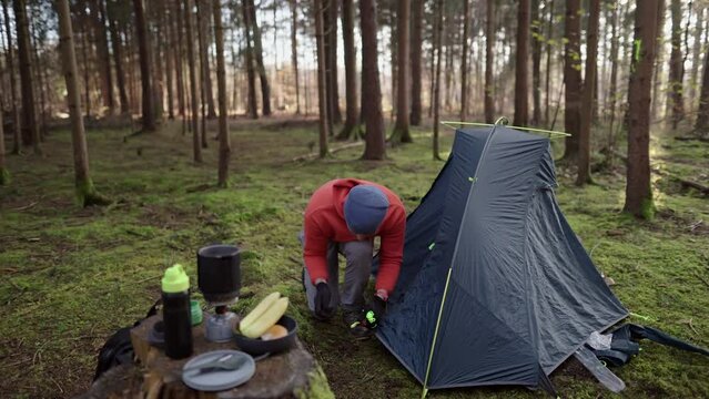 Camping, tourism and travel concept. Man setting up tent outdoors. Hiker assembles campsite tent in the autumnal forest. Traveler installing tent in autumn woods. Outdoor weekend Activity. 