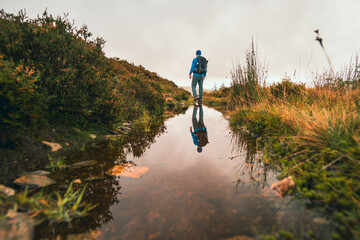 Side view of young male hiker with backpack standing on the rock in forest near water with...