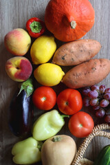 Round straw bag with seasonal fruit and vegetable on wooden background. Late summer or early autumn. Top view.