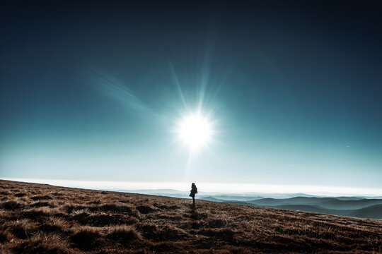 Woman stands on horizon hills with big shinning sun above her head, Krkonose, Czech republic, minimalistic nature scene, blue beautiful skies