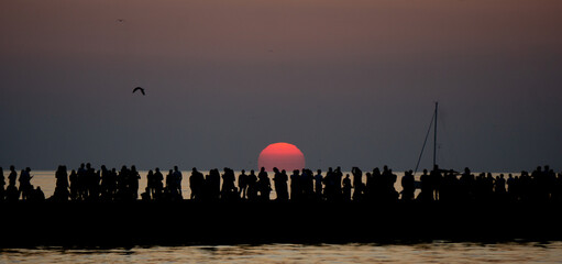 Spectacular sunset with the sun alomst gone and plenty of people on the warf