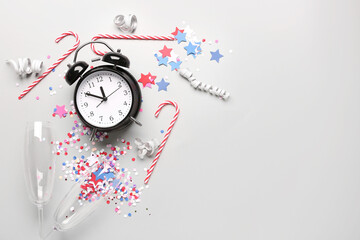 Alarm clock with Christmas candy canes, glasses and confetti on white background