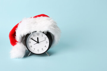 Alarm clock with Santa hat on blue background